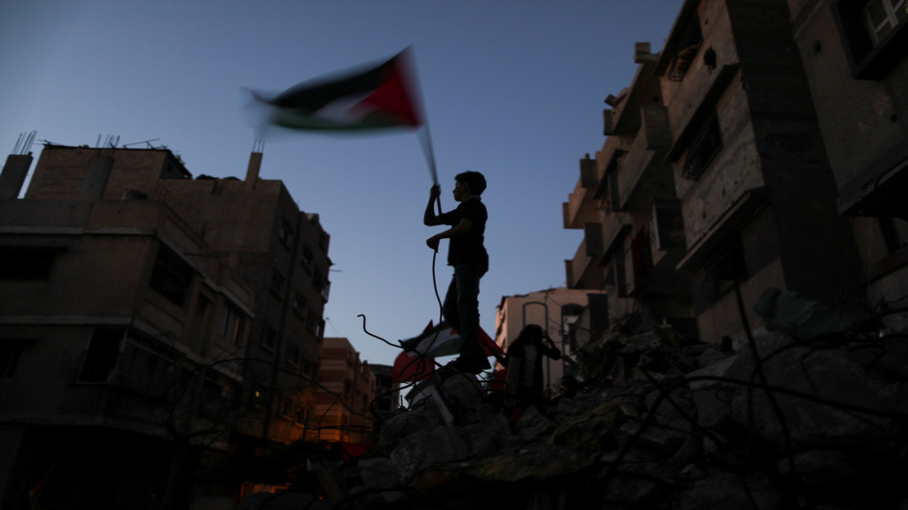 صبي يلوح بالعلم الفلسطيني في موقع تضرر من الغارات الجوية الإسرائيلية في مدينة غزة خلال العدوان الإسرائيلي على القطاع، 23 أيار/مايو 2021. (صهيب سالم/رويترز)