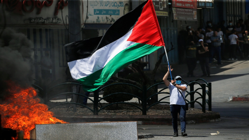 متظاهر يحمل علما فلسطينيا خلال مظاهرة مناهضة لإسرائيل، في الخليل بالضفة الغربية المحتلة، 18 مايو 2021. (رويترز)