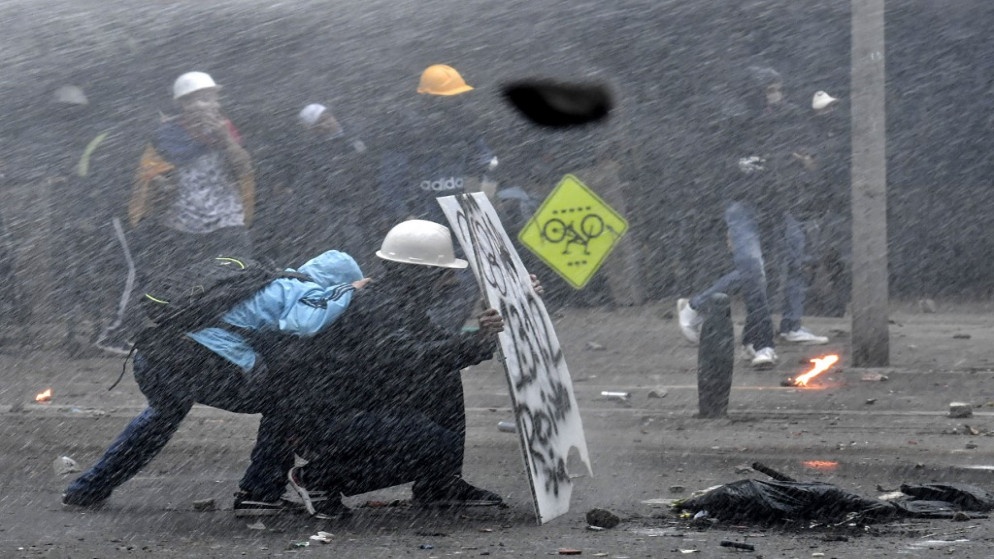متظاهرون يختبئون من خراطيم مياه تابعة لشرطة مكافحة الشغب خلف درع مؤقت خلال اشتباكات في ميديلين، كولومبيا، 28 أيار/مايو 2021. (أ ف ب)