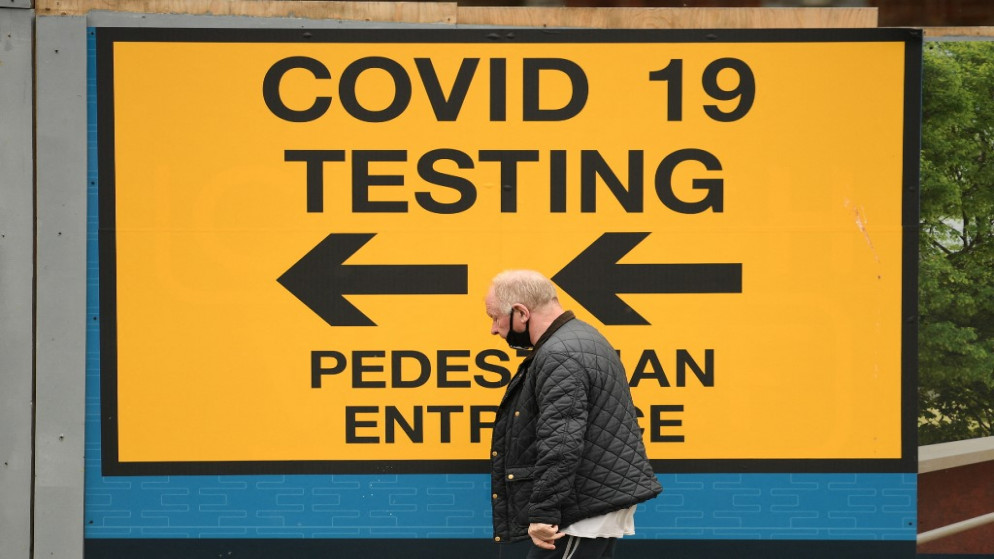 رجل يسير أمام لافتة توجه الجمهور إلى مركز اختبار Covid-19 في بولتون، شمال غرب إنجلترا، 28 مايو 2021. (أ ف ب)