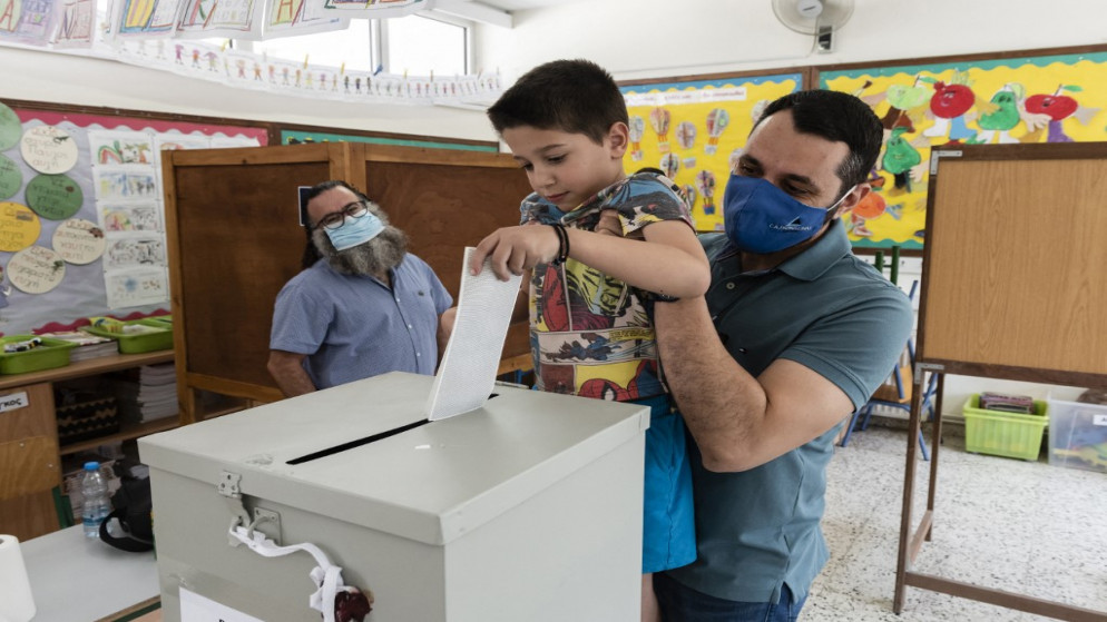 رجل قبرصي يحمل ابنه للإدلاء بصوته في مركز اقتراع في نيقوسيا، 30 مايو 2021. (أ ف ب)