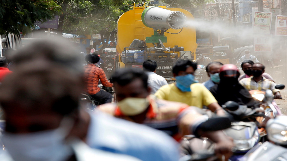 أشخاص يرتدون كمامات واقية للوجه يركبون دراجات نارية بينما تقوم مركبة بلدية برش معقمات في الطريق لإبطاء انتشار فيروس كورونا في الهند. 09/04/2021. (رويترز)
