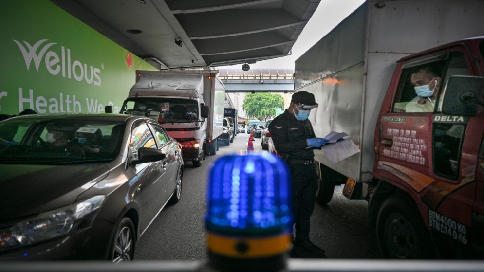 شرطي يتفقد وثائق سفر سائق سيارة عند حاجز طريق أثناء الإغلاق على مستوى البلاد، وسط مخاوف من انتشار فيروس كورونا، في كوالالمبور، 1 يونيو 2021. (رويترز)