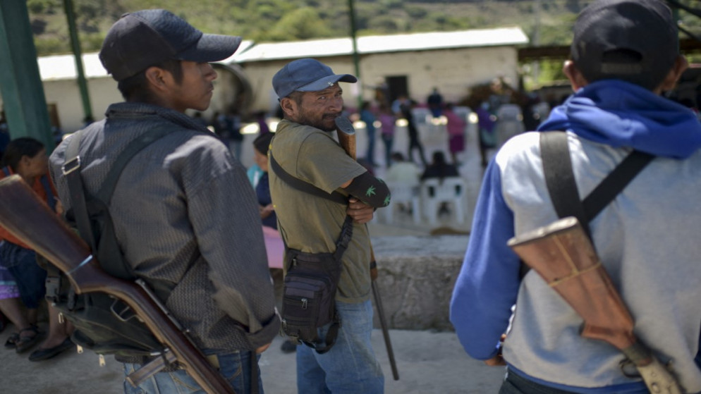 يصطف الناس للإدلاء بأصواتهم بينما يقف أفراد الشرطة المجتمعية في مركز اقتراع في مجتمع ناهوات في آياهوالتمبا، ولاية غيريرو، المكسيك، 6 حزيران/يونيو 2021. (أ ف ب)