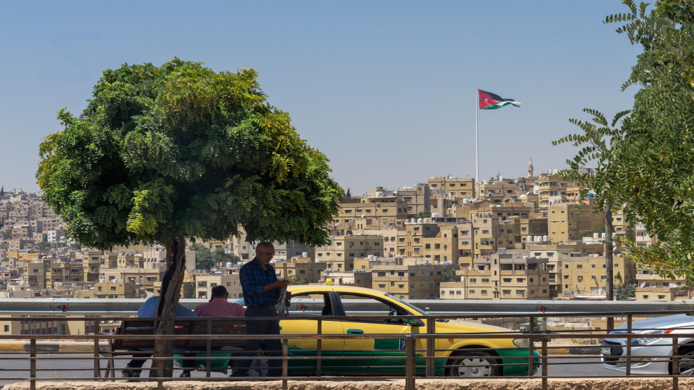 سيارة أجرة تقف في أحد شوارع عمّان وخلفها سارية علم الأردن في قصر رغدان. 01/08/2019. (shutterstock)