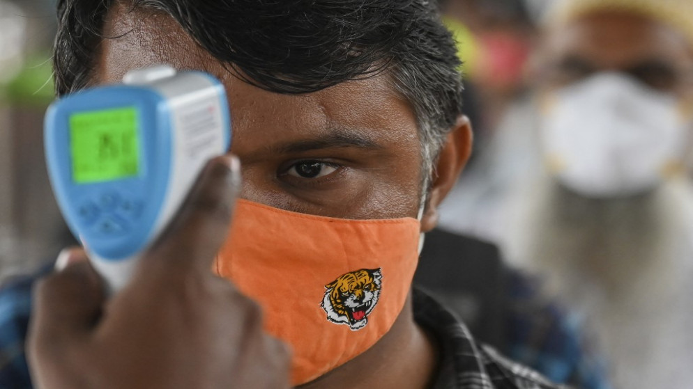 عامل صحي يتحقق من درجة حرارة شخص عند وصوله إلى رصيف للسكك الحديدية، في مومباي، الهند، 8 حزيران/يونيو 2021. (أ ف ب)