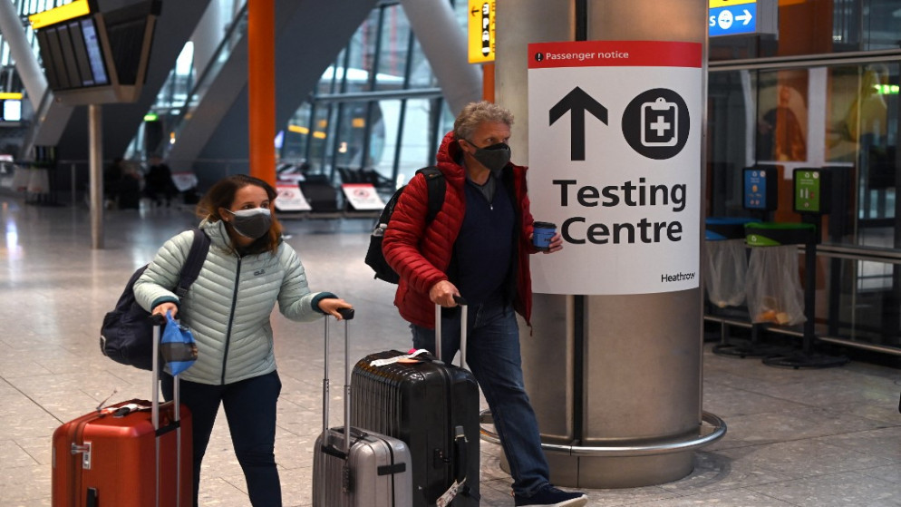 مسافران في مطار في لندن وأمامهما لافتة لإجراء فحص الكشف عن فيروس كورونا. (أ ف ب)