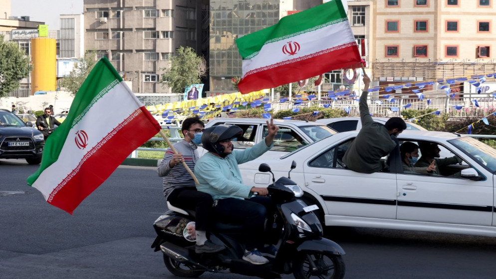 ركاب يلوحون بالأعلام الوطنية يمرون أمام لافتة انتخابية تظهر المرشح الإيراني إبراهيم خلال تجمع حاشد في العاصمة طهران .15 يونيو 2021. (أ ف ب)