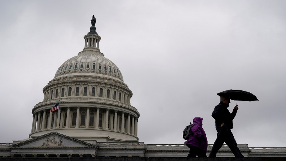 شخصان يسيران أمام الكونغرس الأميركي (رويترز)