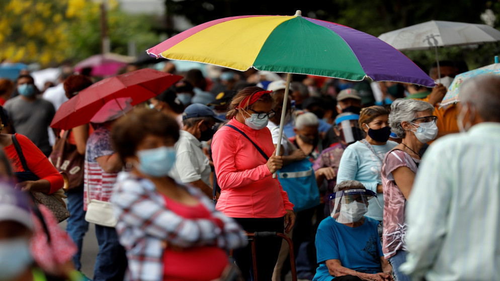 امرأة تحمل مظلة تنتظر مع والدتها، لتلقي جرعتها الأولى من اللقاح المضاد للفيروس، في ماراكاي، فنزويلا، 8 يونيو/حزيران ، 2021. (رويترز)