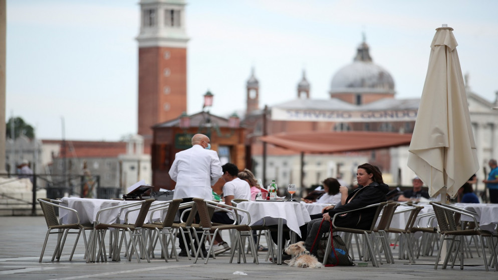يجلس الناس في مطعم بميدان سانت مارك، حيث أصبحت منطقة فينيتو "منطقة بيضاء"، بعد تخفيف قيود مرض فيروس كورونا، مع الأقنعة فقط والتباعد الاجتماعي، البندقية، إيطاليا، 7 يونيو/حزيران 2021. (رويترز)
