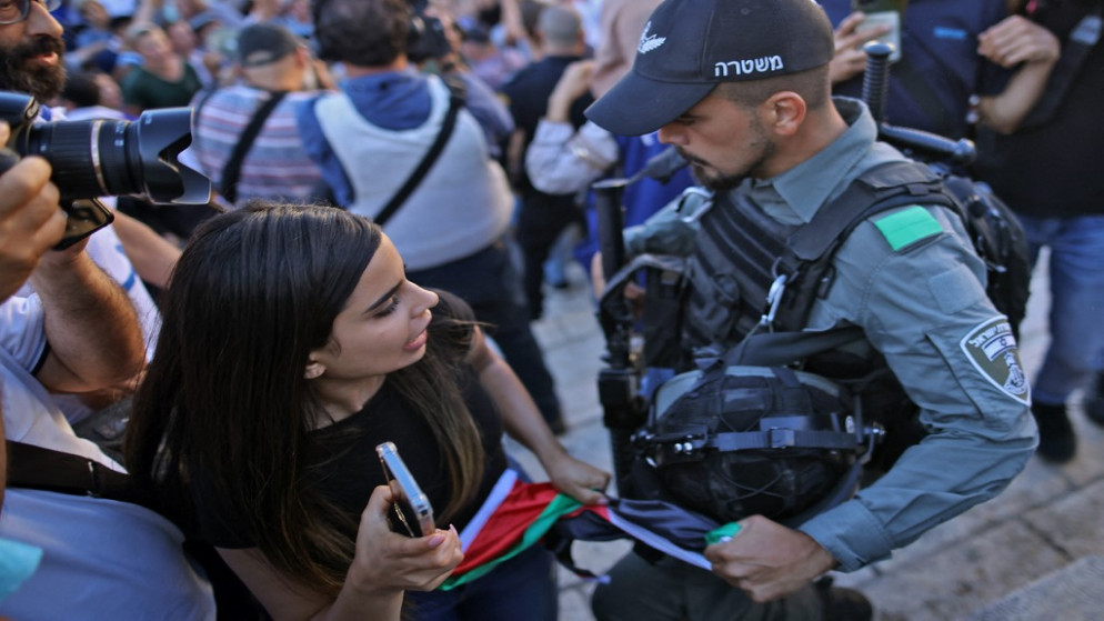 جندي إسرائيلي يصادر العلم الفلسطيني من يد فلسطينية بينما يشارك متطرفون إسرائيليون في مسيرة الأعلام قرب البلدة القديمة في القدس. 15/06/2021. (حمد غرابلي / أ ف ب)
