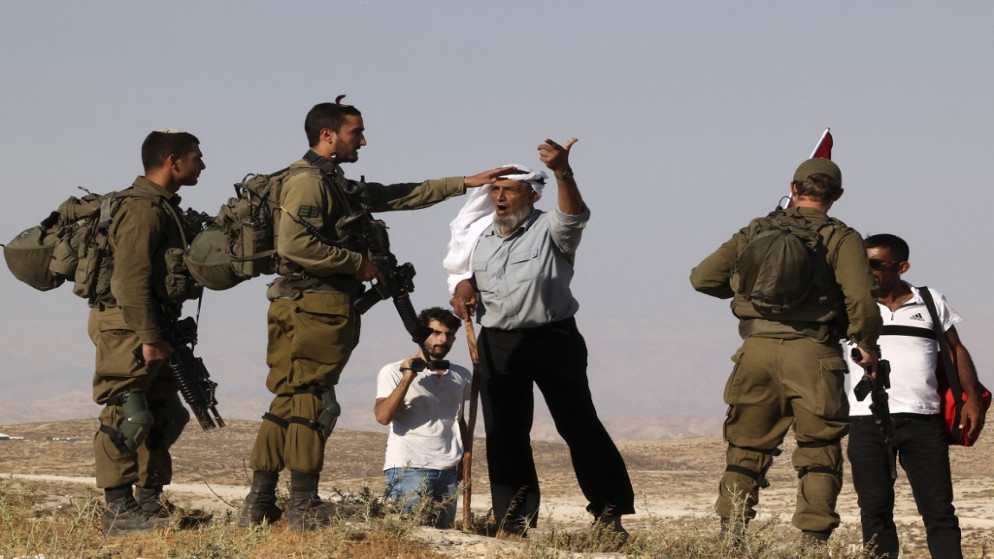 قوات الاحتلال الإسرائيلي بعد تأمين مسيرة للمستوطنين في الضفة الغربية المحتلة وخلال حديثها مع مسن فلسطيني. (أ ف ب)