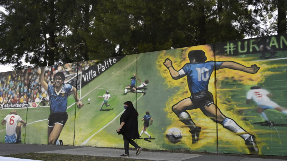 امرأة تسير بجانب حائط وضع عليه صور النجم الأرجنتيني دييغو مارادونا خلال هدفه الشهير في كأس العالم عام 1986. (أ ف ب)