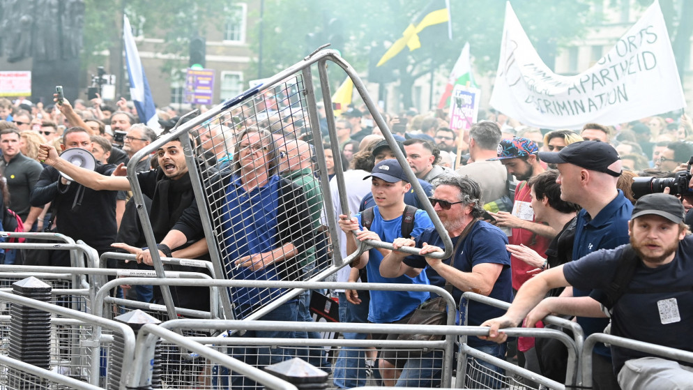 أشخاص يلقون سياجًا خلال مظاهرة مناهضة للقاح والإغلاق خارج داونينج ستريت وسط لندن. 26 يونيو 2021. (أ ف ب)