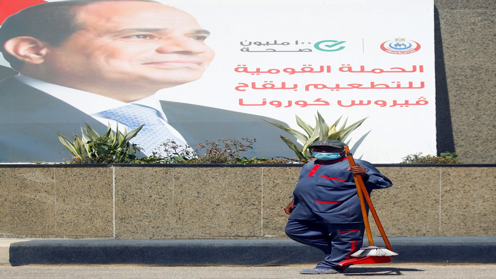 عامل ينظف أمام ملصق للرئيس المصري عبد الفتاح السيسي كتب عليه "الحملة الوطنية للقاح فيروس كورونا"، القاهرة، مصر، 2 يونيو 2021. (رويترز)