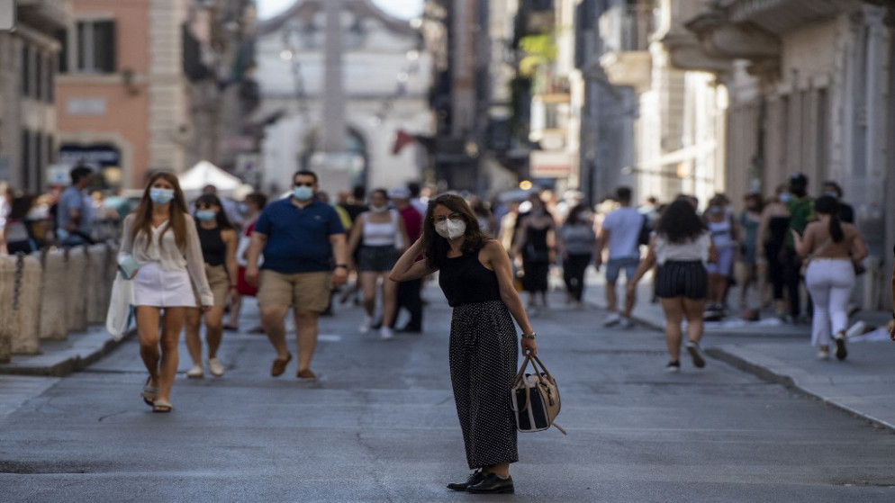 أشخاص يسيرون في شارع بإيطاليا متجهين إلى منطقة في روما لا توجب ارتداء كمامات الوقاية من كورونا في الهواء الطلق. 27/06/2021. (أ ف ب)