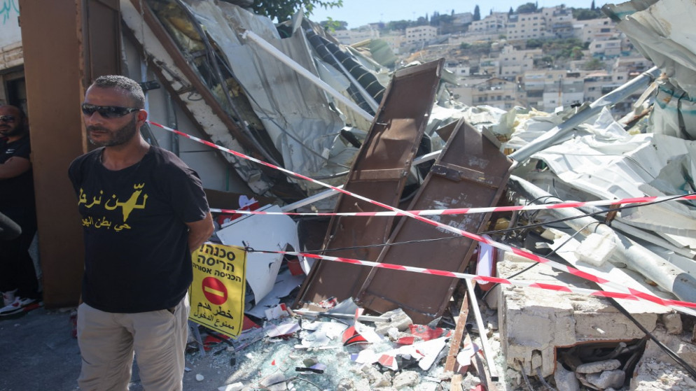 فلسطيني يرتدي قميصا كتب عليه عبارة "لن نرحل" يقف بجوار أنقاض متجر هدمته سلطات الاحتلال الإسرائيلية في حي سلوان . 29/06/2021. (أحمد غرابلي / أ ف ب)