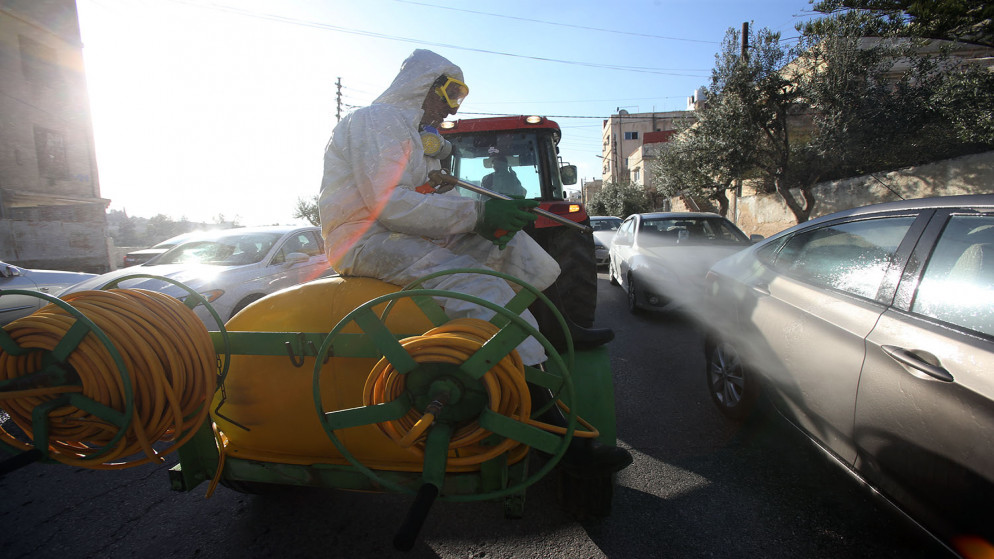 صورة أرشيفية لشخص يعمل على تعقيم مركبة في حي سكني جرى إغلاقه بعد تسجيل إصابات بكورونا فيه. (صلاح ملكاوي/المملكة)