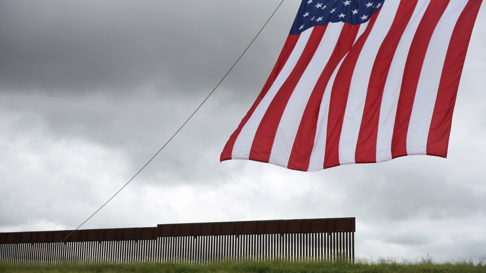 علم الولايات المتحدة يرفرف أمام جزء من الجدار الحدودي بين الولايات المتحدة والمكسيك في فار، تكساس، الولايات المتحدة، 30 يونيو 2021. (رويترز)