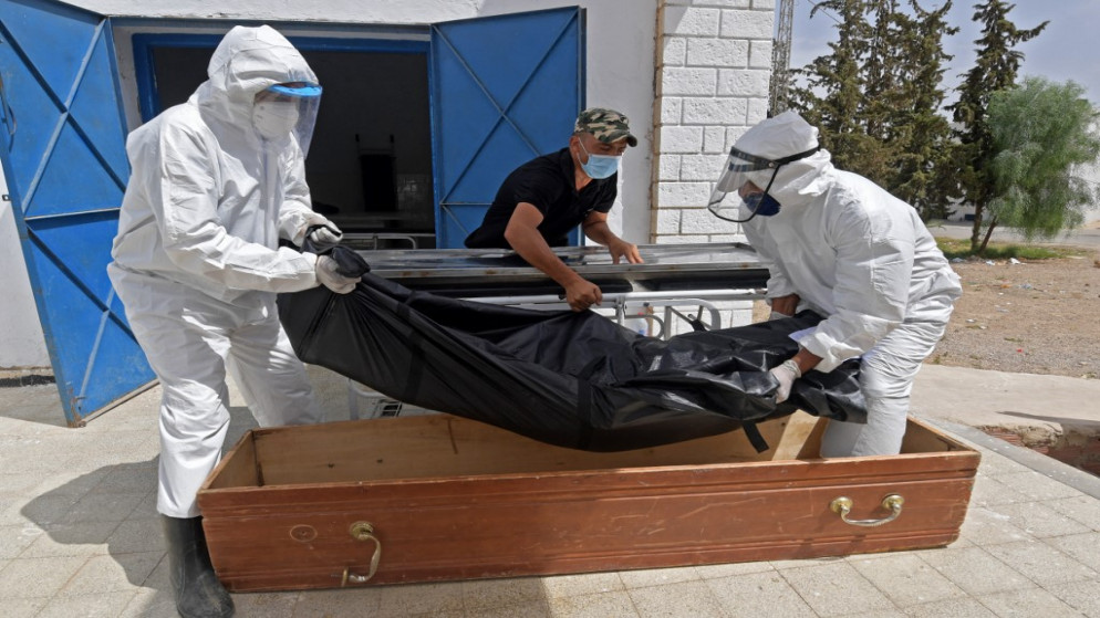 موظفو البلدية التونسية يضعون جثة أحد ضحايا فيروس كورونا في تابوت في مستشفى ابن الجزار في شرق وسط مدينة القيروان، 4 تموز/يوليو 2021. (أ ف ب)