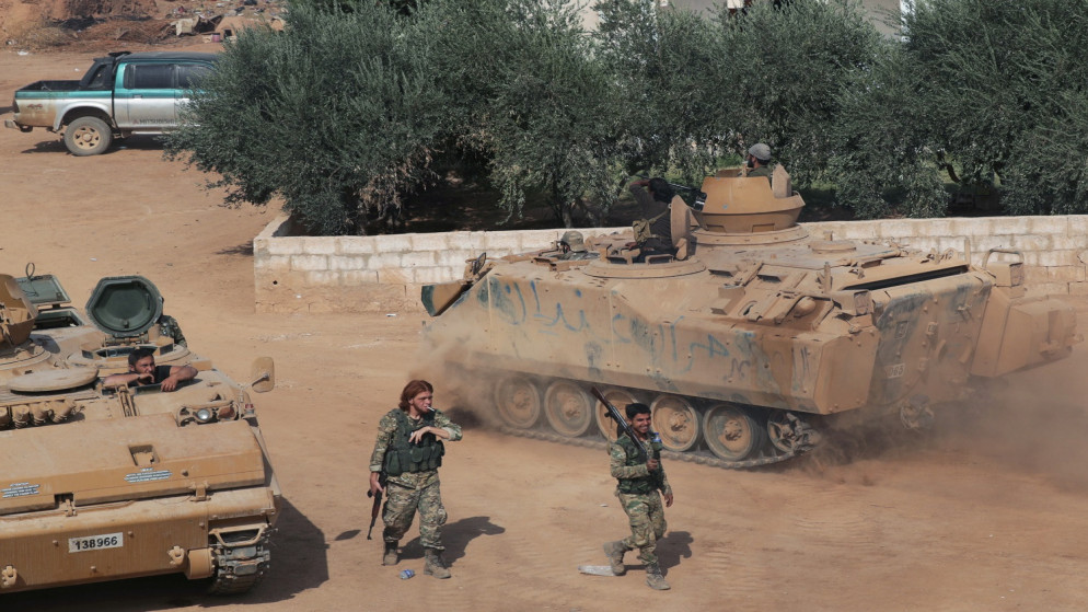 مقاتلون سوريون مدعومون من تركيا يمرون بالقرب من دبابات عسكرية أثناء تجمعهم بالقرب من بلدة تل أبيض الحدودية.(رويترز)
