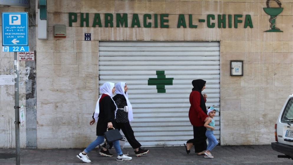 أشخاص يمشون أمام باب مغلق لصيدلية في العاصمة اللبنانية بيروت ، خلال إضراب على مستوى البلاد للصيدليات احتجاجًا على النقص الحاد في الأدوية. 9 يوليو / تموز 2021.(أ ف ب)