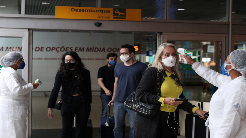 عاملة صحية تقيس درجة حرارة مسافر في حاجز صحي أثناء وصولها مع آخرين إلى مطار كونجونهاس في ساو باولو بالبرازيل، 31 أيار/مايو 2021. (رويترز)