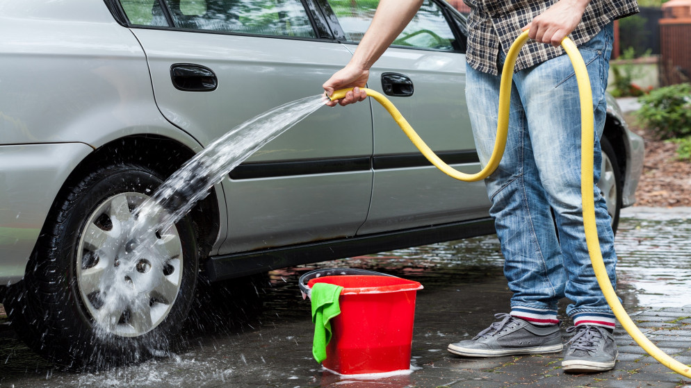 صورة توضيحية لشخص يغسل مركبته بخرطوم مياه. (shutterstock)