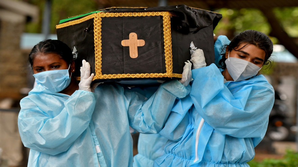 متطوعتان تحملان جثة شخص مات بسبب فيروس كورونا لدفنه في مقبرة في بنغالورو، الهند، 18 أيار/مايو 2021 (رويترز)