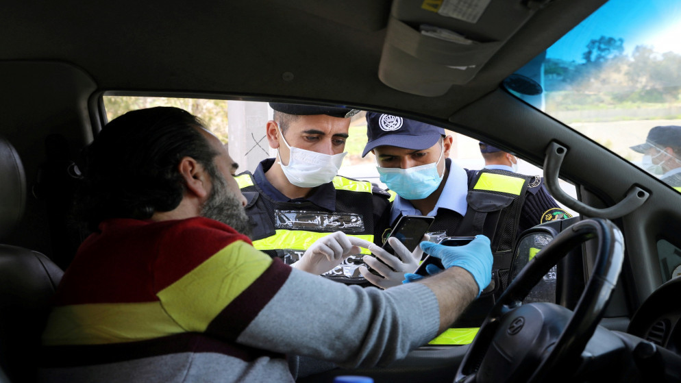 صورة أرشيفية لرجال أمن يفحصون تصريحا إلكترونيا للمرور لسائق مركبة وسط مخاوف من انتشار فيروس كورونا في الأردن. 08/04/2020. (محمد حامد/ رويترز)