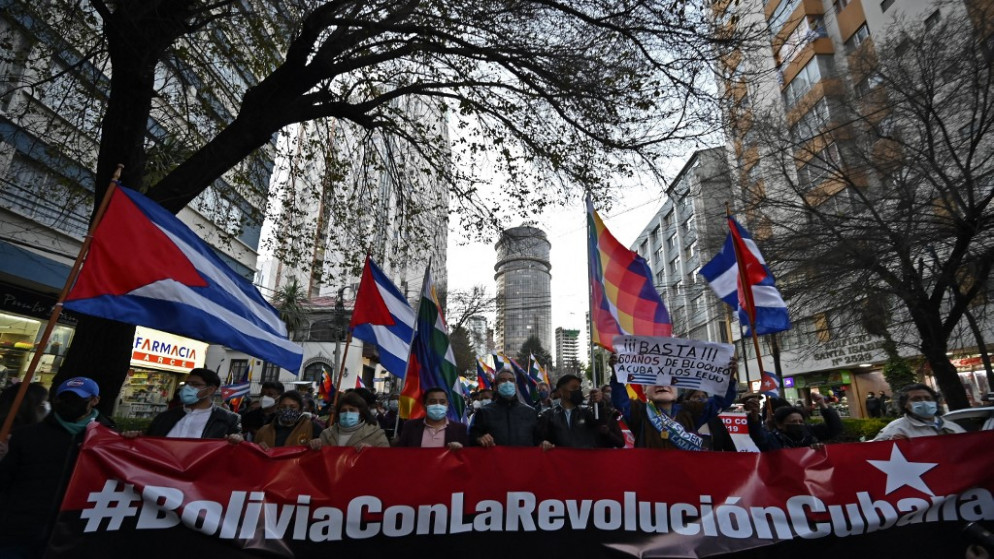 أنصار الرئيس البوليفي، يتظاهرون مع العلمين الكوبيين وويفالا- ممثلين لشعوب جبال الأنديز- ولافتة كتب عليها "بوليفيا مع الثورة الكوبية"، خارج السفارة الأميركية في لا باز، 14 يوليو 2021. (أ ف ب)
