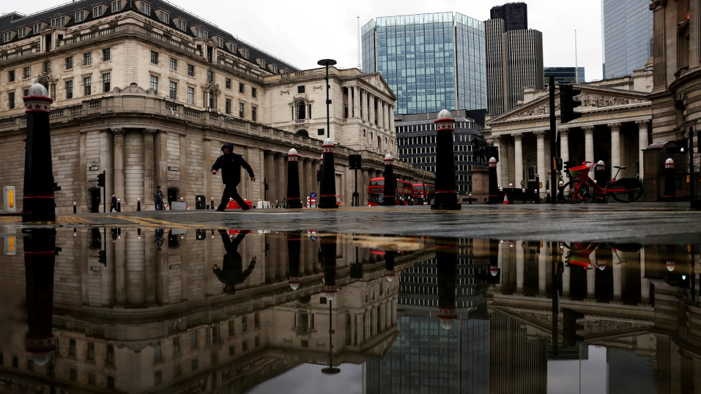 بنك إنجلترا ورويال إكستشينج ينعكسان في بركة مياه بينما يمر أحد المارة وسط تفشي فيروس كورونا، لندن، بريطانيا، 19 تشرين الثاني/ نوفمبر 2020. (رويترز)