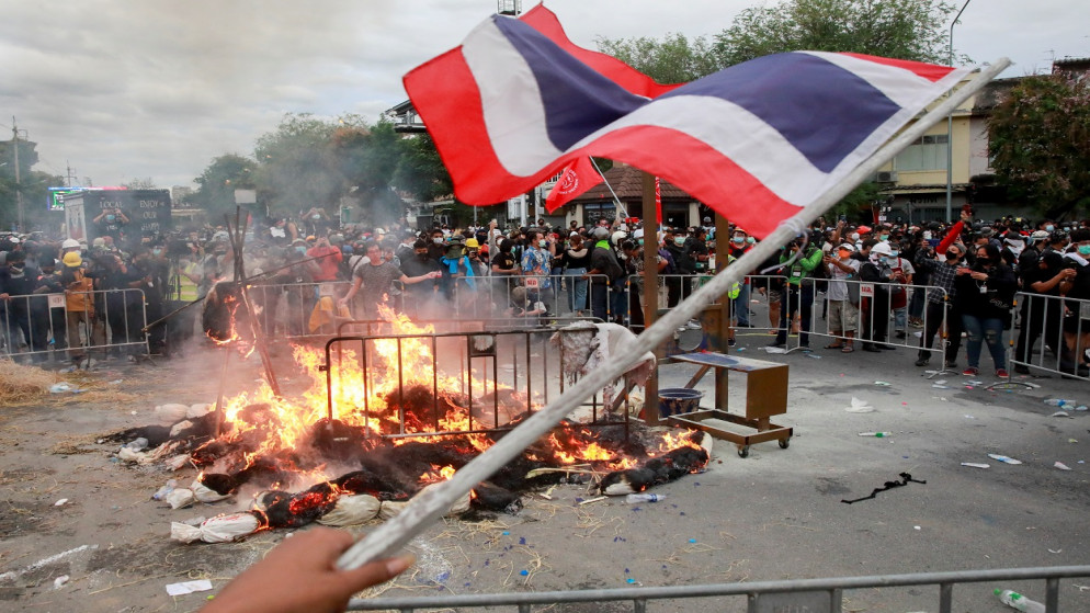 أحد المتظاهرين يلوح بعلم تايلاند وهم يحرقون أكياس جثث وهمية، تمثل نتيجة مرض فيروس كورونا، خلال تظاهرة مناهضة للحكومة، في بانكوك، تايلاند، 18 تموز/يوليو 2021. (رويترز)