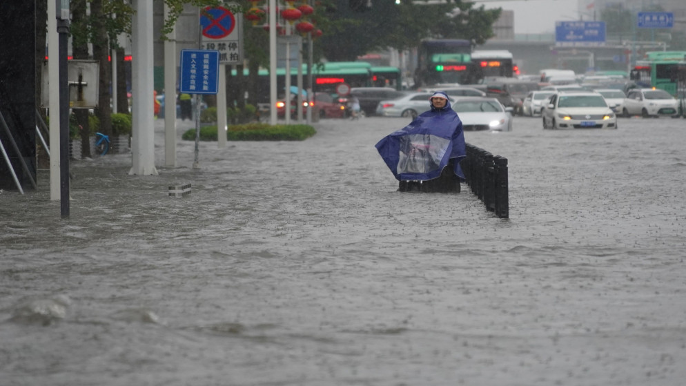 شخص يرتدي غطاء مطر يقف على طريق غمرته المياه في مدينة تشنغتشو بمقاطعة خنان، الصين، 20 تموز/يوليو 2021 (رويترز)