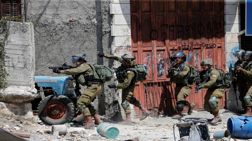 جندي تابع للاحتلال الإسرائيلي يلقي قنبلة صوتية خلال تشييع جنازة طفل فلسطيني، بالقرب من مدينة الخليل بالضفة الغربية المحتلة في 29 يوليو / تموز 2021. (رويترز)