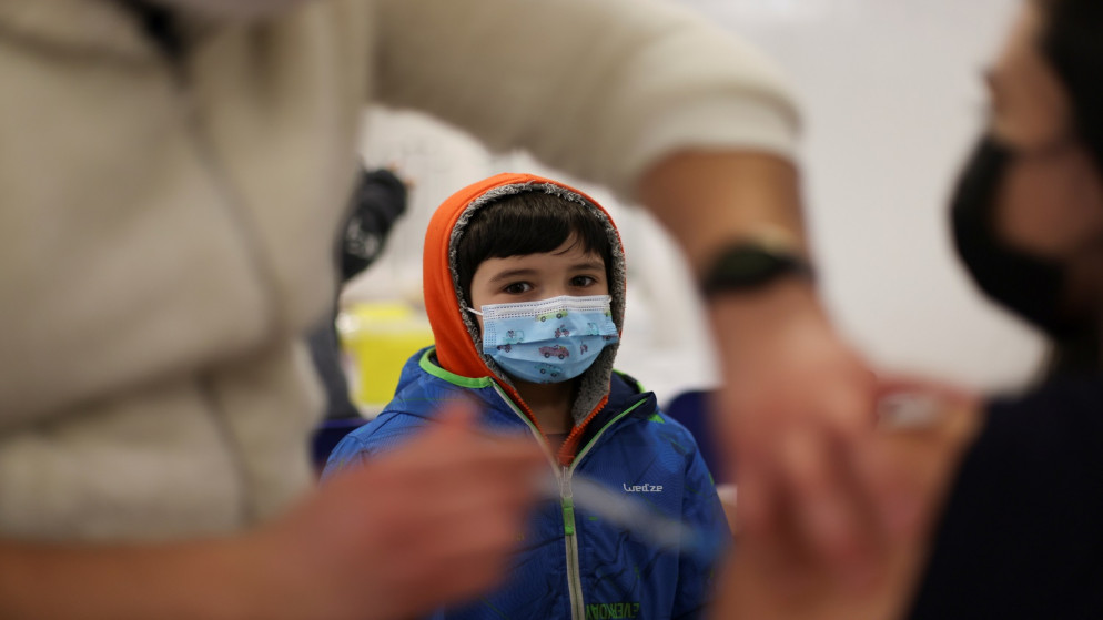 طفل ينظر إلى شخص يتلقى لقاح واقي من فيروس كورونا. (رويترز)