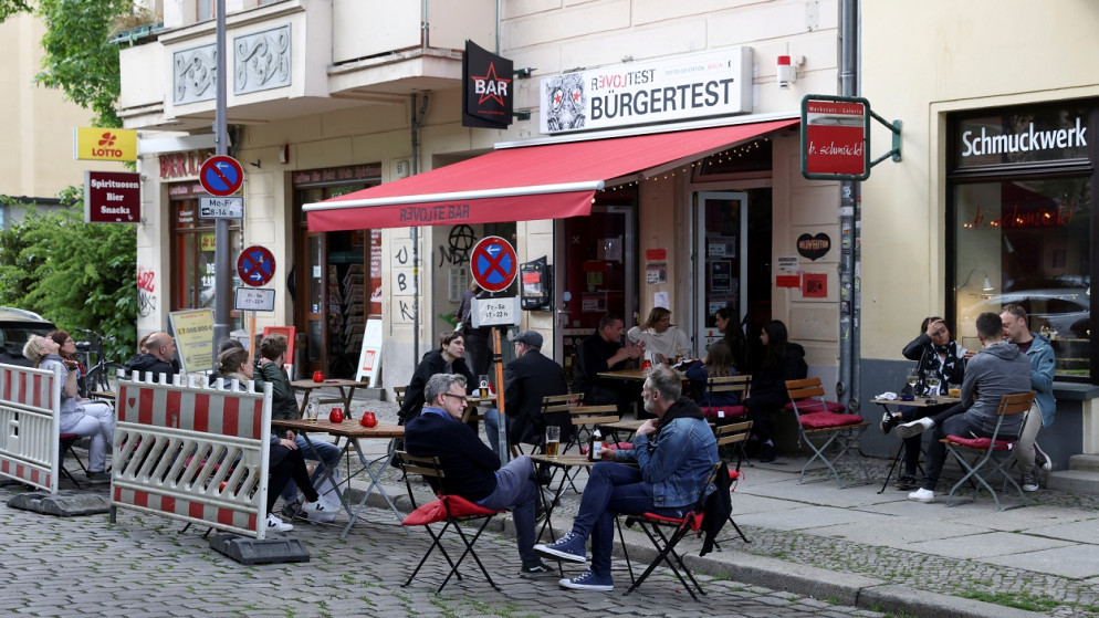 يستمتع الناس بمشروباتهم على باب مقهى، حيث تعيد المقاهي والمطاعم فتح شرفاتها بعد إغلاقها لعدة أشهر وسط تفشي فيروس كورونا، برلين، ألمانيا، 21 أيار/مايو 2021. (رويترز)