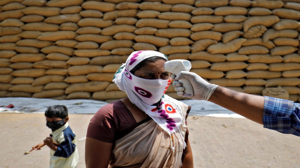 عامل رعاية صحية يفحص درجة حرارة عاملة في مطحنة أرز في قرية بافلا في ضواحي أحمد أباد، الهند، 13 أبريل / نيسان 2021. (رويترز / أميت ديف)