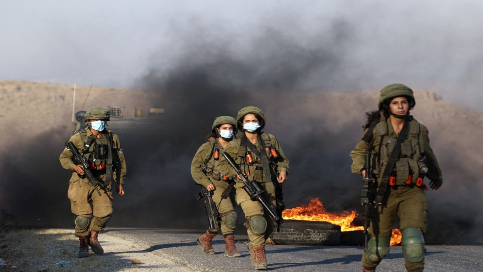 جنود إسرائيليون يمرون بالقرب من الإطارات المحترقة أثناء انتشارهم لتفريق المتظاهرين الفلسطينيين بالقرب من معسكر للجيش الإسرائيلي تم إخلاؤه سابقًا والذي سيطر عليه المستوطنون عند حاجز تياسير شرق طوباس شمال الضفة الغربية المحتلة .31 يوليو، 2021.(أ ف ب)