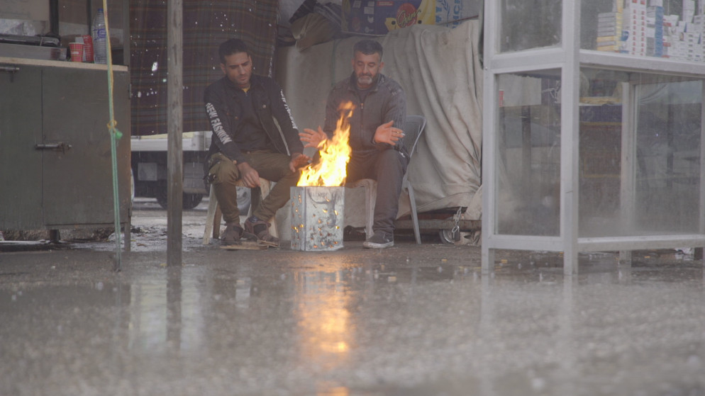 رجلان يجلسان بجانب مدفأة صنعاها من الحطب في شارع فرعي بمخيم البقعة في عمّان. (فادي اسكندراني/المملكة)