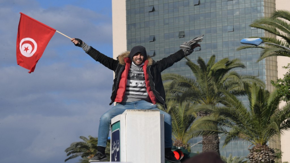 متظاهر تونسي يلوح بالعلم الوطني لبلاده خلال الاحتجاجات ضد الرئيس قيس سعيد، في الذكرى 11 للثورة التونسية في العاصمة تونس، 14 كانون الثاني/يناير 2022. (أ ف ب)