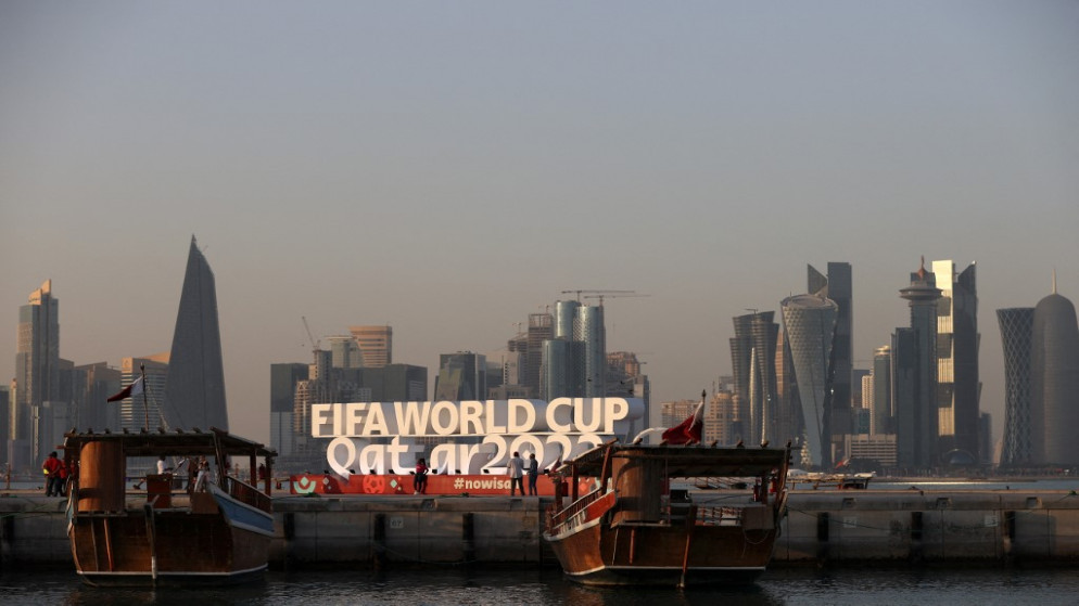 زوارق تحمل علم قطر مقابل شعار عليه عبارة كأس العالم 2022 قطر. (أ ف ب)