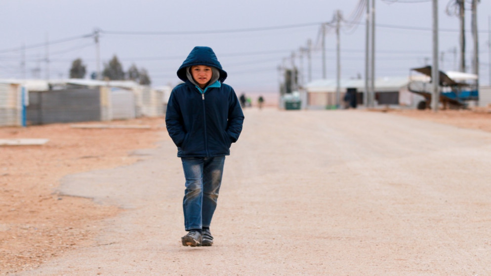 طفل سوري يضع يديه في ملابسه للوقاية من البرد يسير في أحد شوارع مخيم الزعتري بمحافظة المفرق. (مفوضية الأمم المتحدة للاجئين)