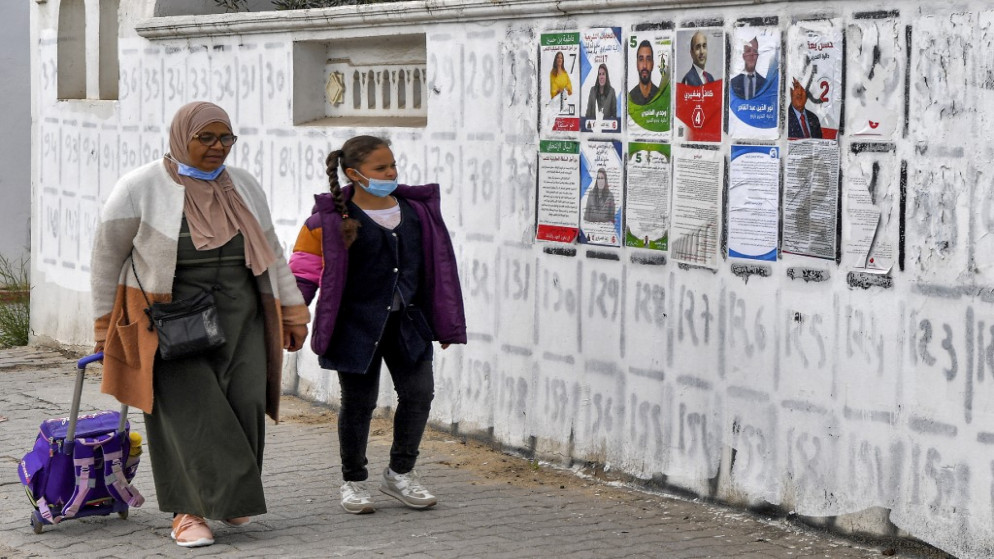 طالبة ووالدتها تسيران أمام ملصقات انتخابية للمرشحين في الانتخابات التشريعية التونسية المقرر إجراؤها في 17 كانون الأول/ديسمبر. 14/12/2022. (فتحي بلعيد /أ ف ب)