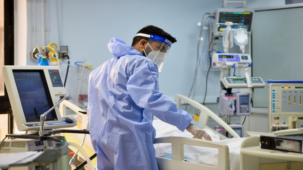 أحد أعضاء الطاقم الطبي يساعد مريضًا في وحدة العناية المركزة في مستشفى في عمان، 23 آذار/مارس 2021. (رويترز)