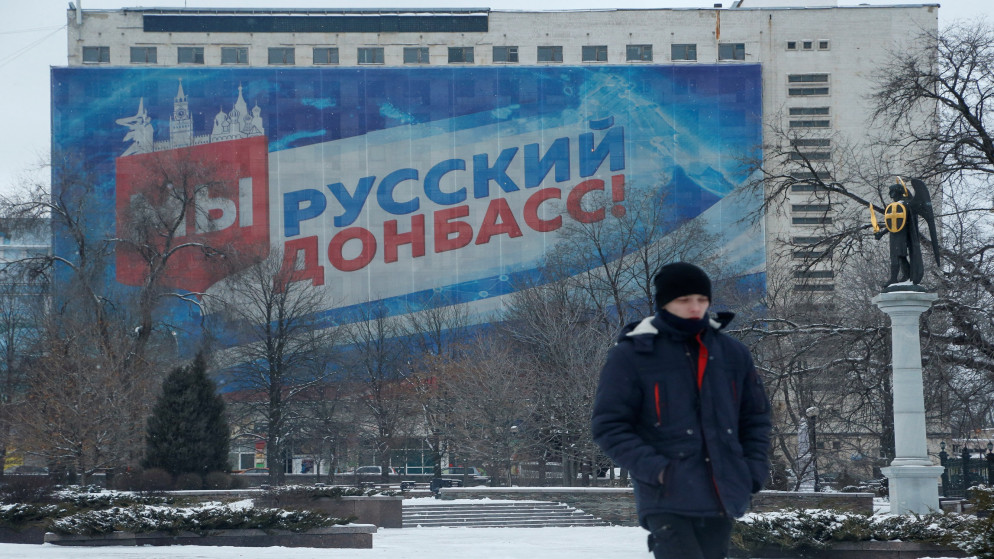 شخص يسير عند ميدان بالقرب من لافتة تحمل شعار "نحن دونباس روسيا!" في مدينة دونيتسك التي تضم أغلبية متمردة في أوكرانيا. 24 كانون الثاني/يناير 2022. (رويترز)