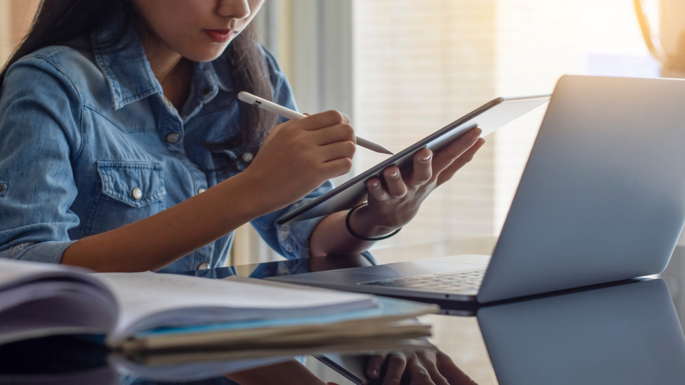 صورة توضيحية لطالبة تدرس عبر كتابها وجهاز لوحي للتعليم عن بعد. (shutterstock)