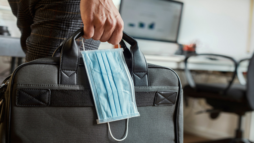 صورة توضيحية لشاب في مكان عمله يحمل حقيبة وكمامة للوقاية من فيروس كورونا. (Shutterstock)