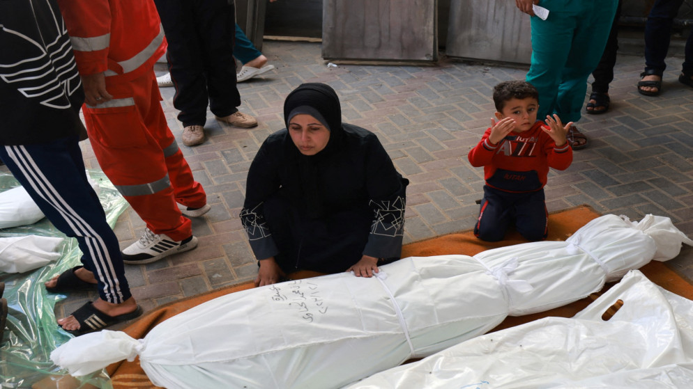 طفل يجلس بجوار فلسطينية أثناء محاولتها العثور على جثة أحد أفراد أسرتها. 1 ديسمبر 2023. (أ ف ب)